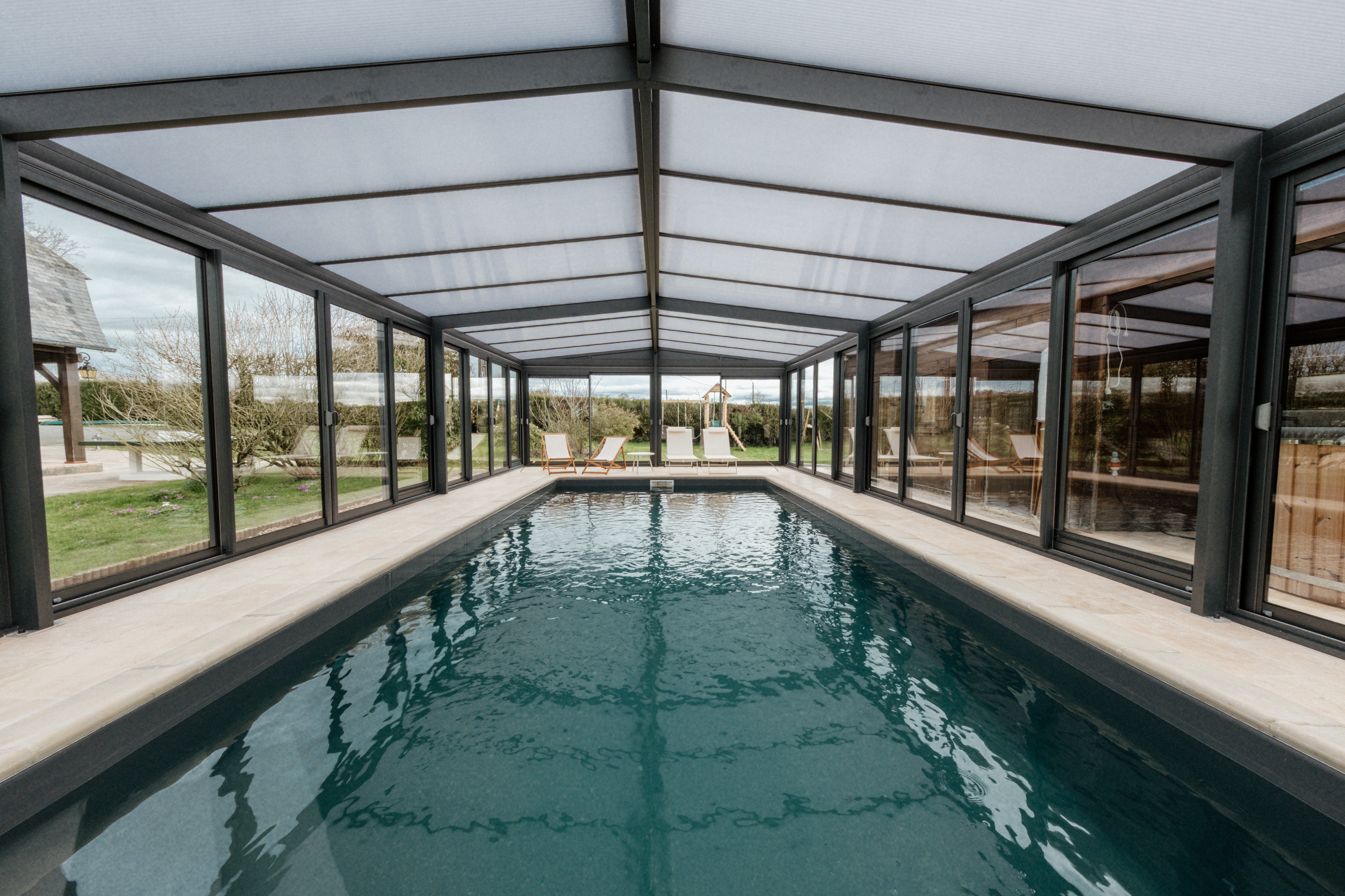 Symmetrical interior of a covered indoor pool with glass walls and a peaked translucent roof