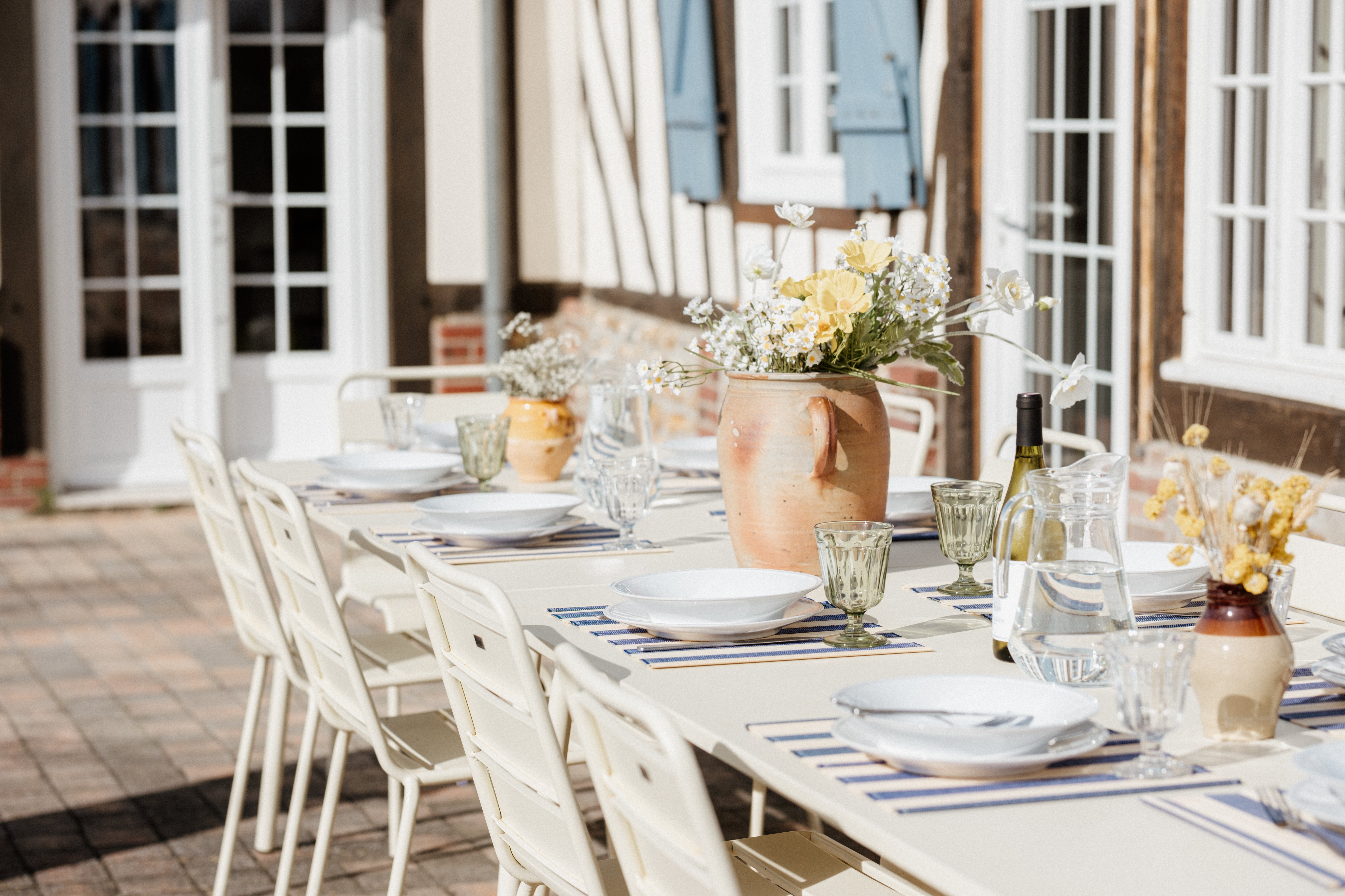 Outdoor dining table set on a half-timbered Normandy farmhouse terrace, soft daylight