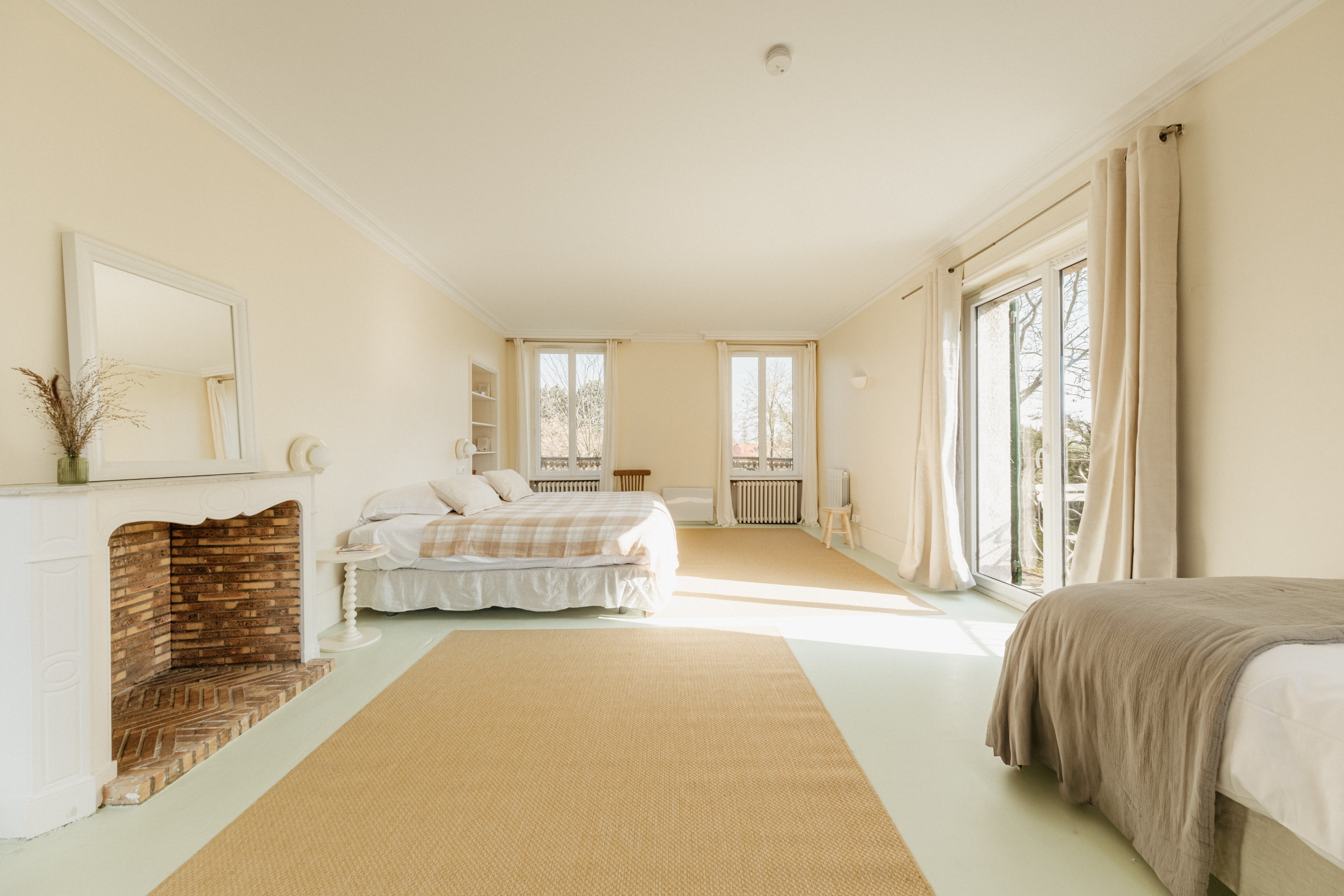 Spacious cream-walled bedroom with a white brick fireplace, checked-canopy bed and tall windows