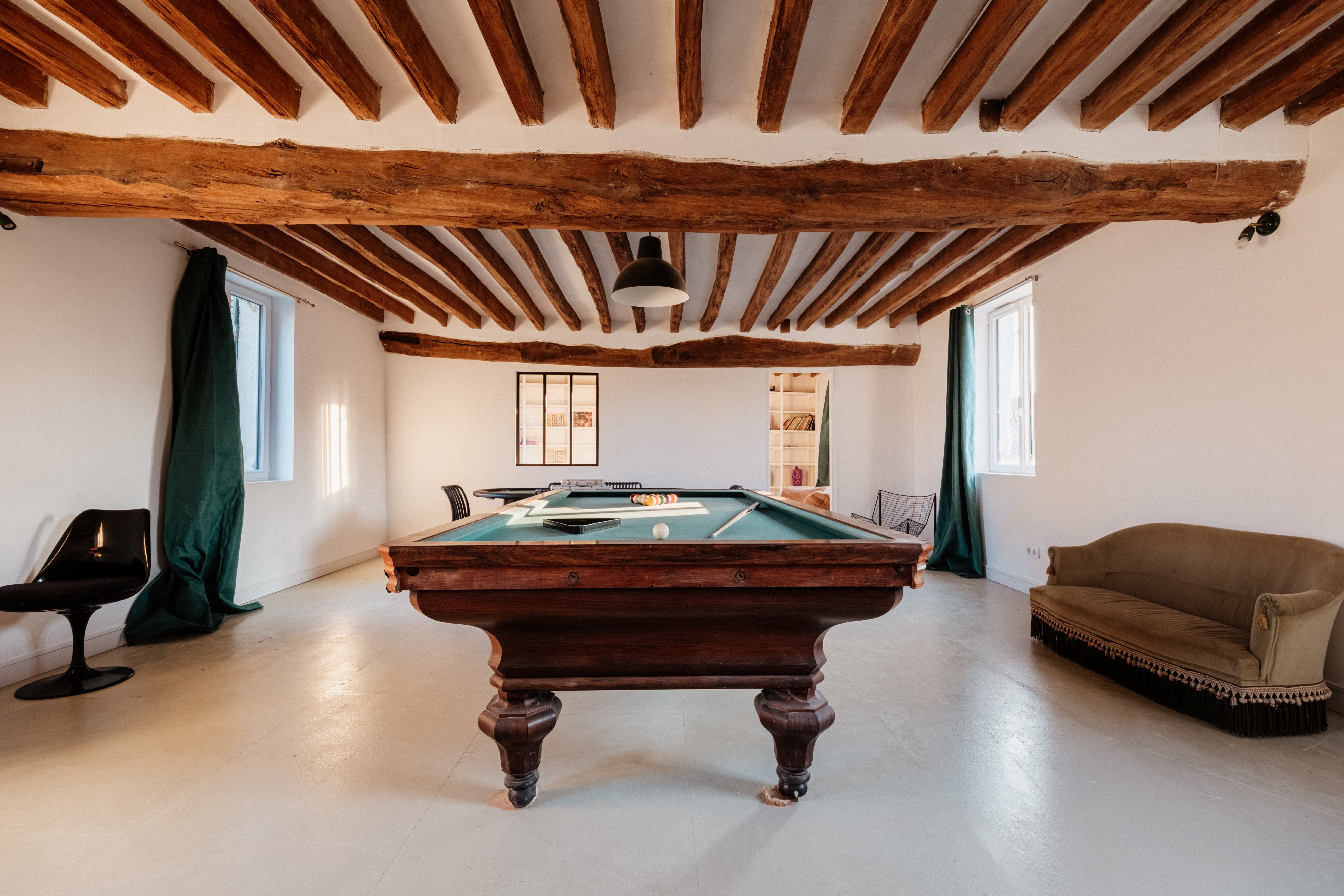 Games room centered on an antique billiard table with green felt under heavy exposed beams