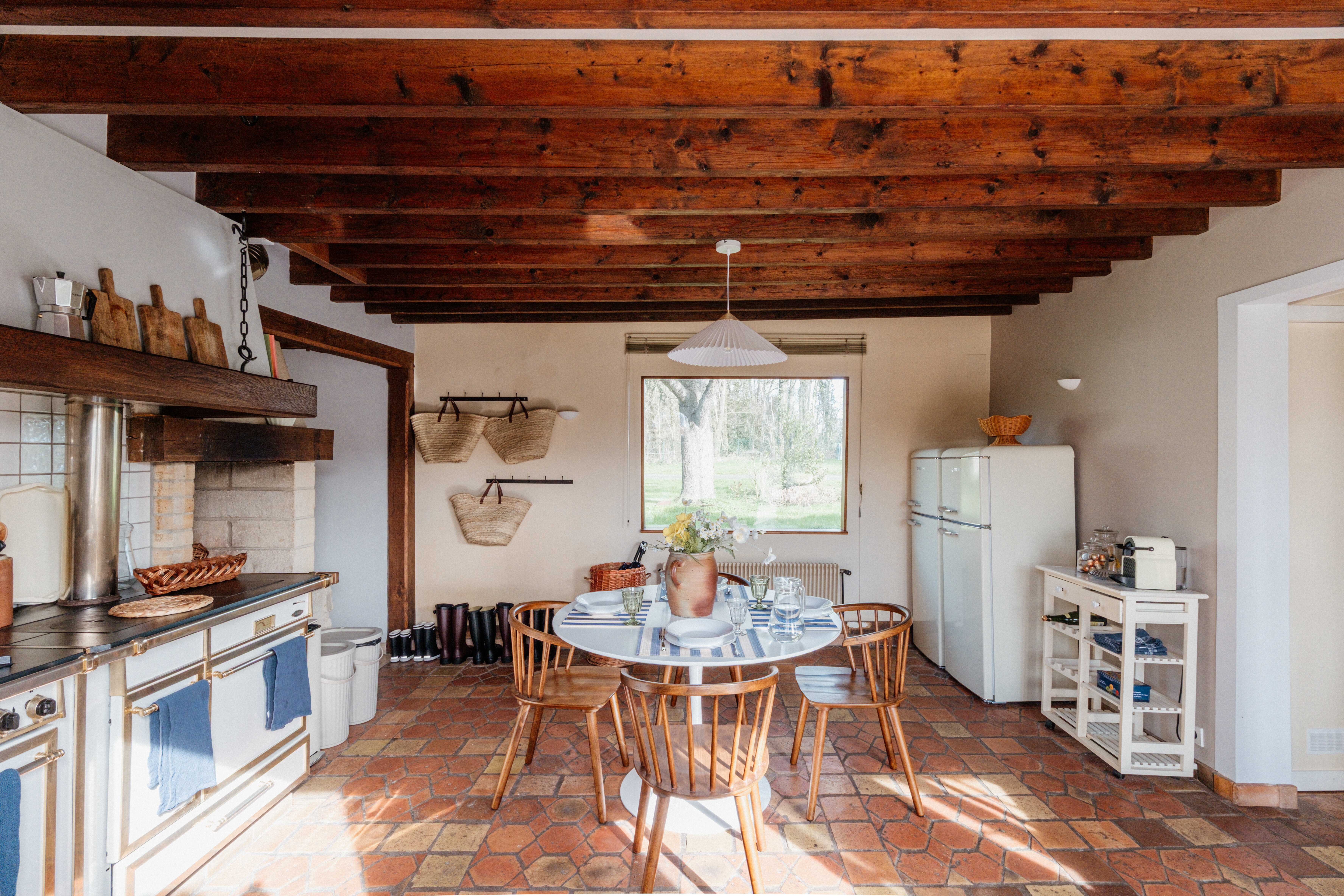 Rustic country kitchen with terracotta tile floor, exposed beams, vintage range and a round wooden table