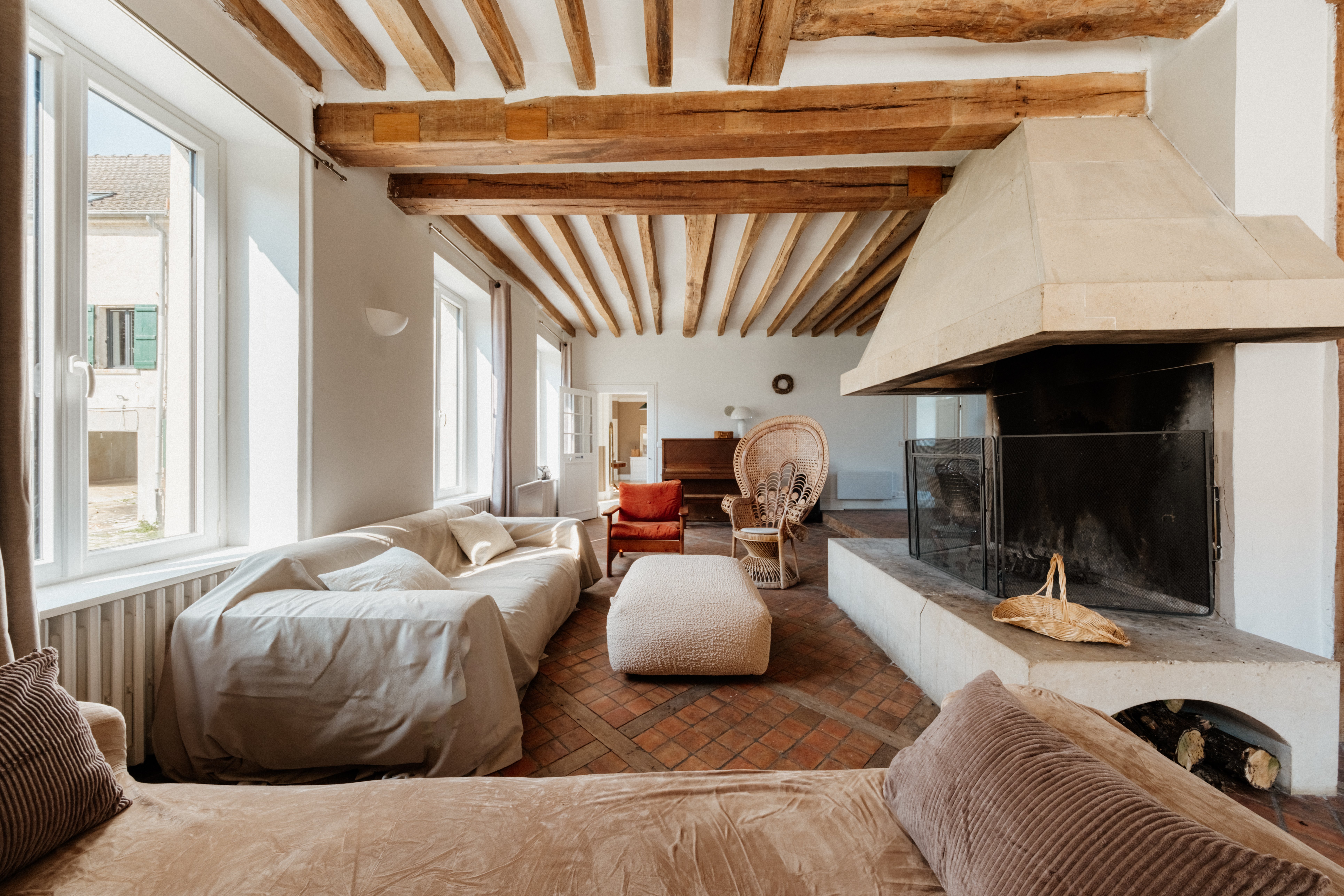 Rustic living room with exposed beams, linen sofas, a stone-hooded fireplace and terracotta tile floor